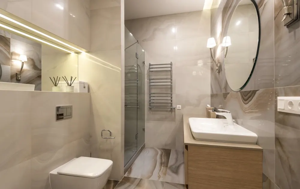 Baño con espejo redondo, apliques de latón y mueble de madera con lavabo sobre encimera