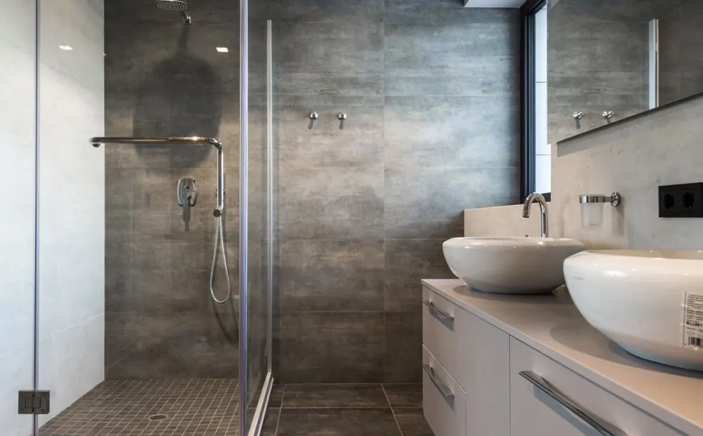 Baño con ducha de obra, doble lavabo sobre encimera y revestimiento efecto piedra