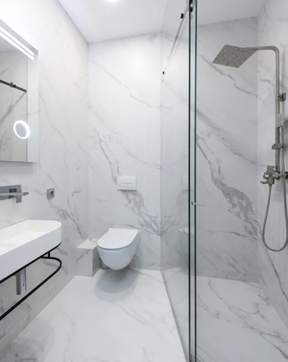 Baño blanco con ducha de obra, mampara de vidrio y lavabo suspendido con toallero