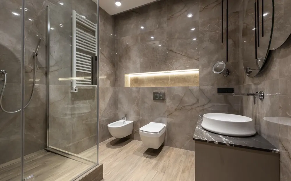 Baño en porcelánico gris con hornacina iluminada, ducha acristalada y sanitarios suspendidos