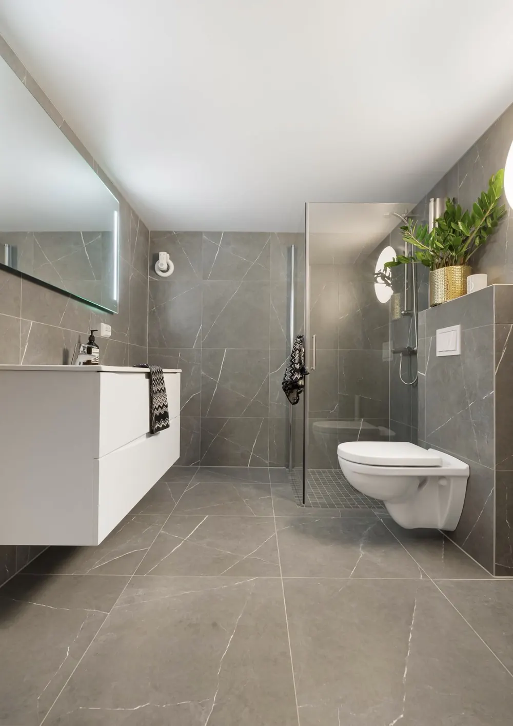 Baño en gris con plato de ducha a ras de suelo, mueble blanco suspendido y espejo con luz