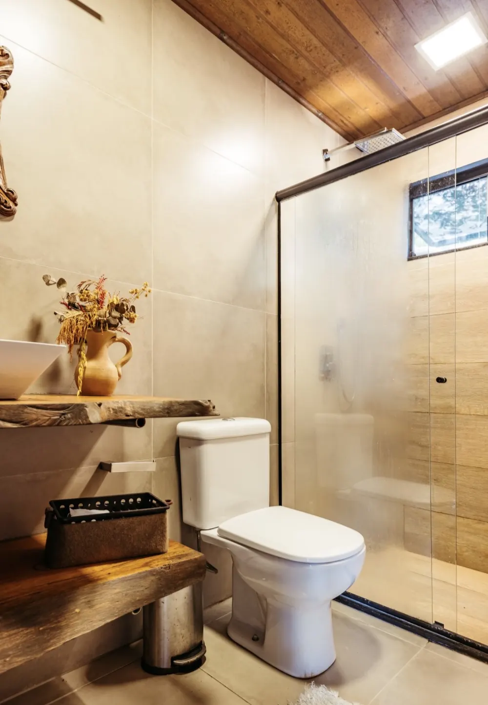 Baño cálido con techo de madera, encimera de tronco y mampara de vidrio