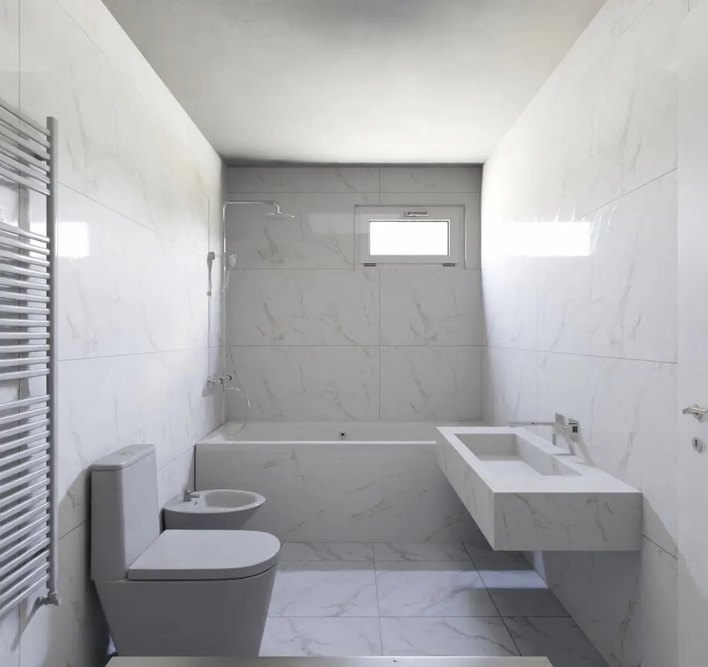 Baño revestido de porcelánico efecto mármol con bañera, lavabo de obra y radiador toallero