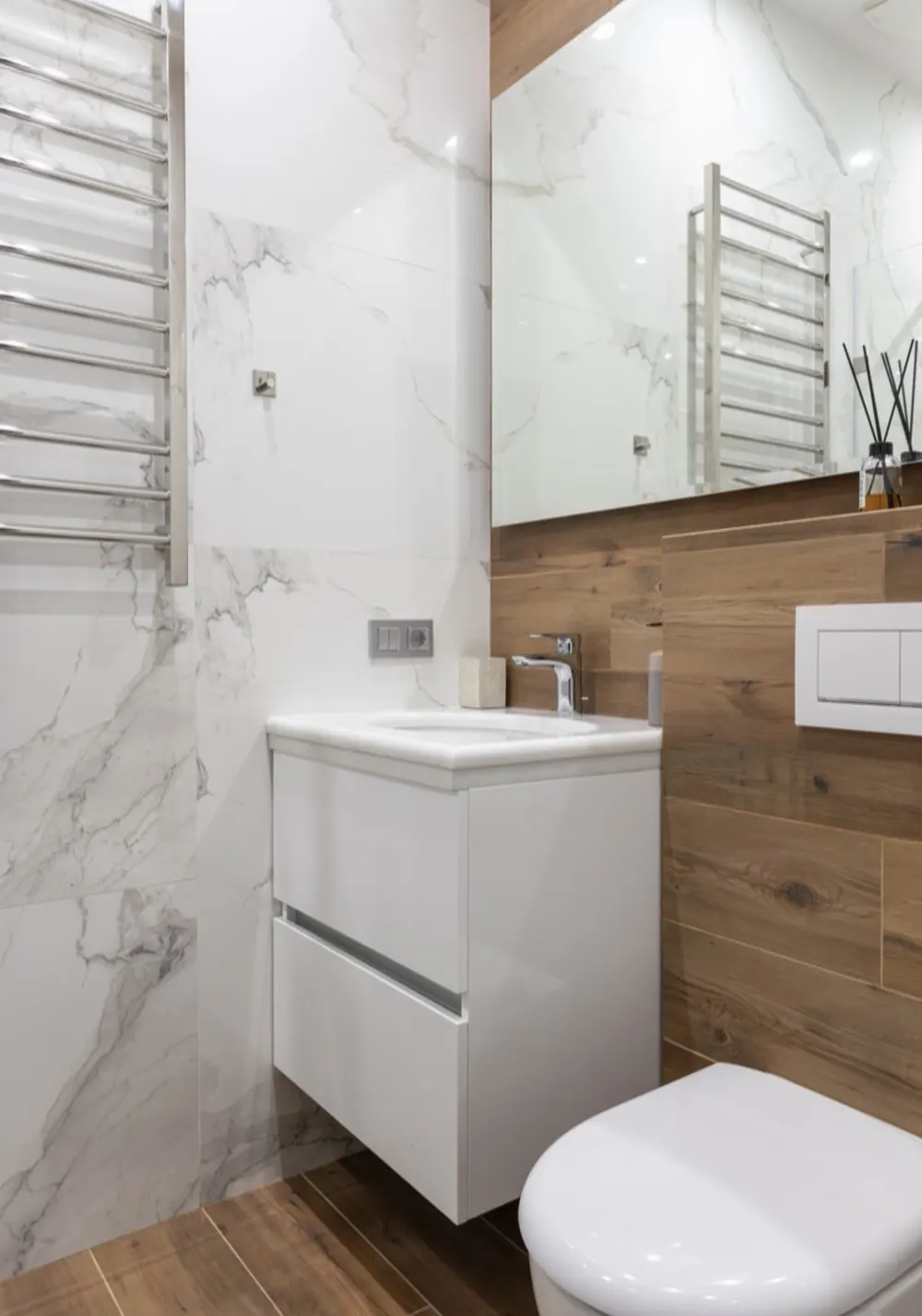 Baño que combina porcelánico efecto mármol y madera, con inodoro suspendido y toallero