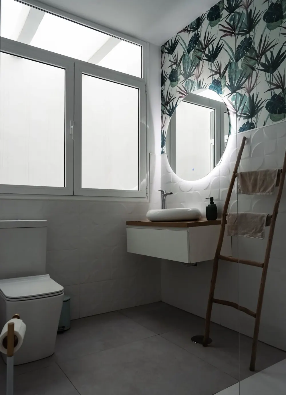 Baño con papel pintado botánico, espejo retroiluminado y mueble volado de madera