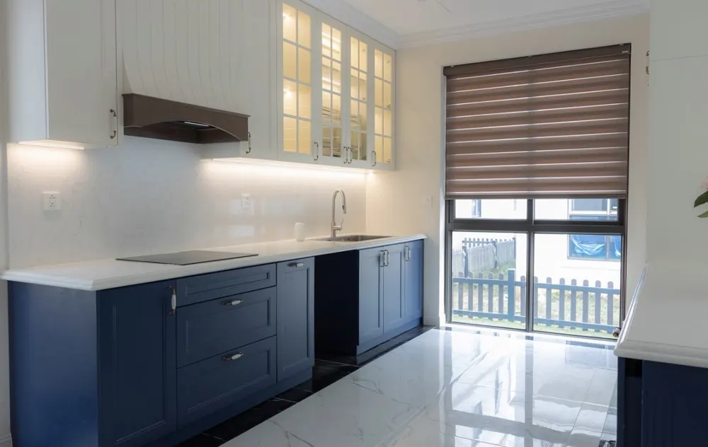 Cocina con muebles azul marino, vitrinas iluminadas y suelo porcelánico brillo