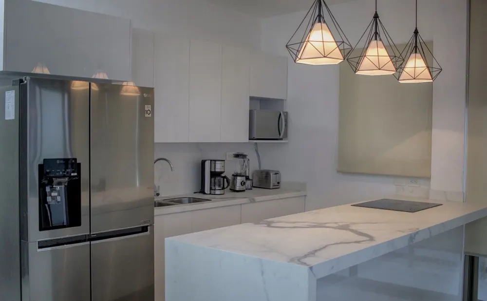 Cocina blanca con península de mármol, frigorífico americano y lámparas de diseño