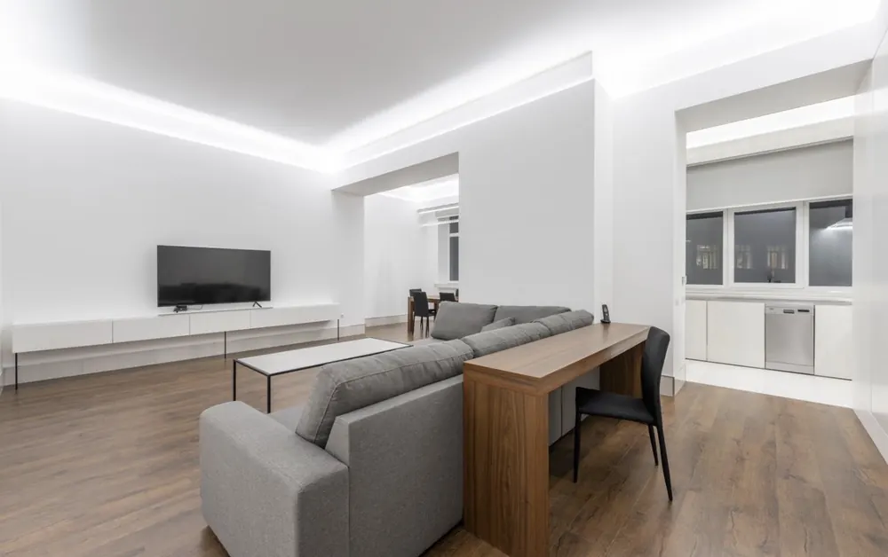 Salón abierto a la cocina tras redistribución, con tira LED perimetral y suelo de madera continuo